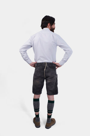 back view of a bearded man standing confidently in Black Forest Lederhosen, complete with knee-high socks and traditional shoes.
