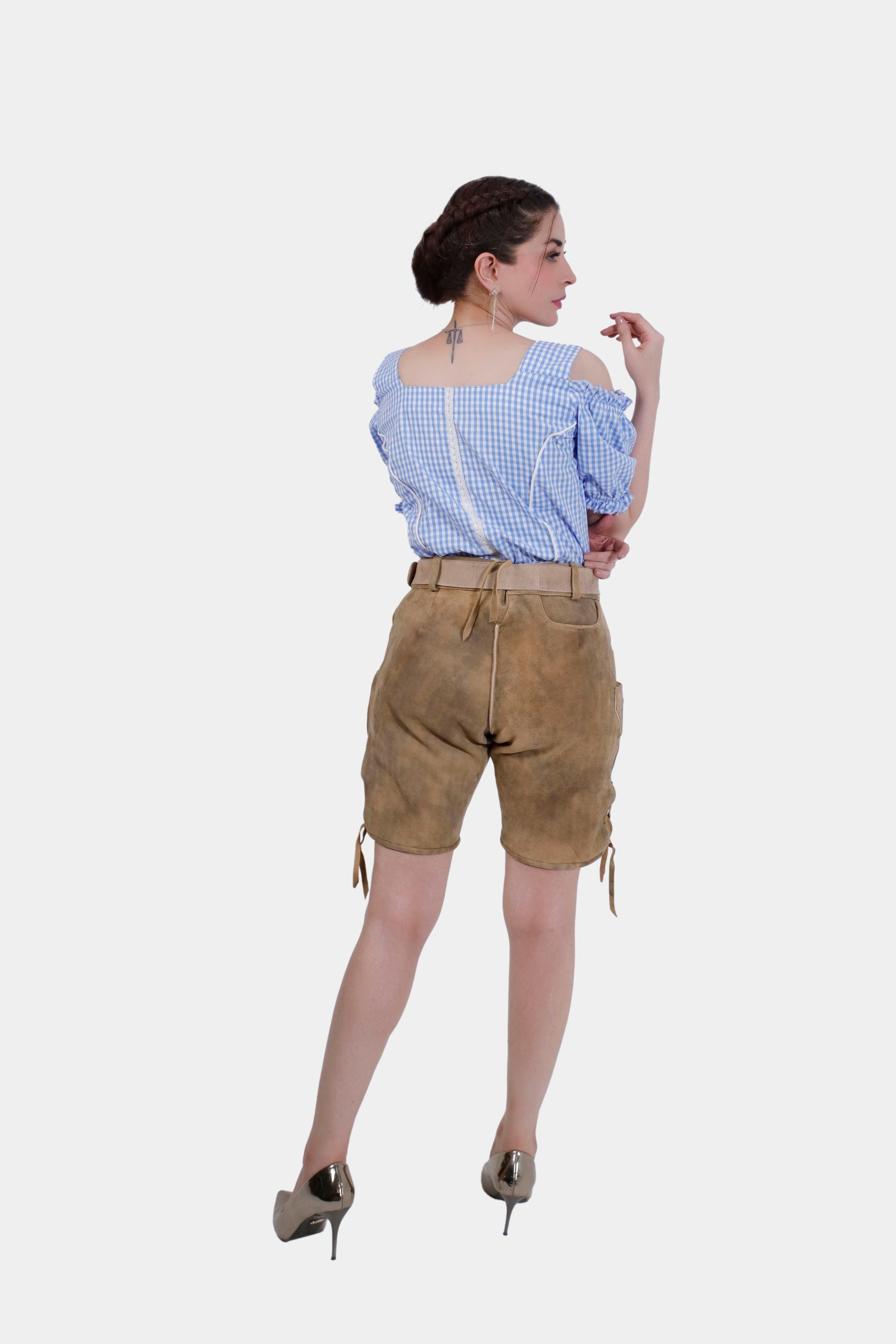 A rear back view of a woman wearing tan leather lederhosen with blue embroidery, showcasing the back pockets and lace-up details, paired with a blue and white checkered blouse.