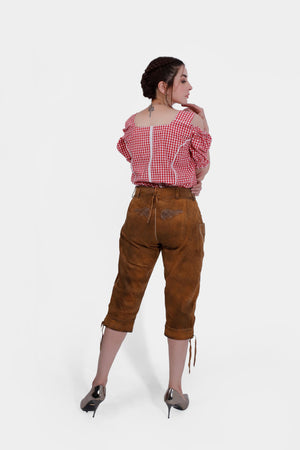 A rear view of a woman in a red checkered off-shoulder blouse and brown leather lederhosen. She is looking to the side, showing off the back embroidery on the lederhosen and wearing metallic high heels.