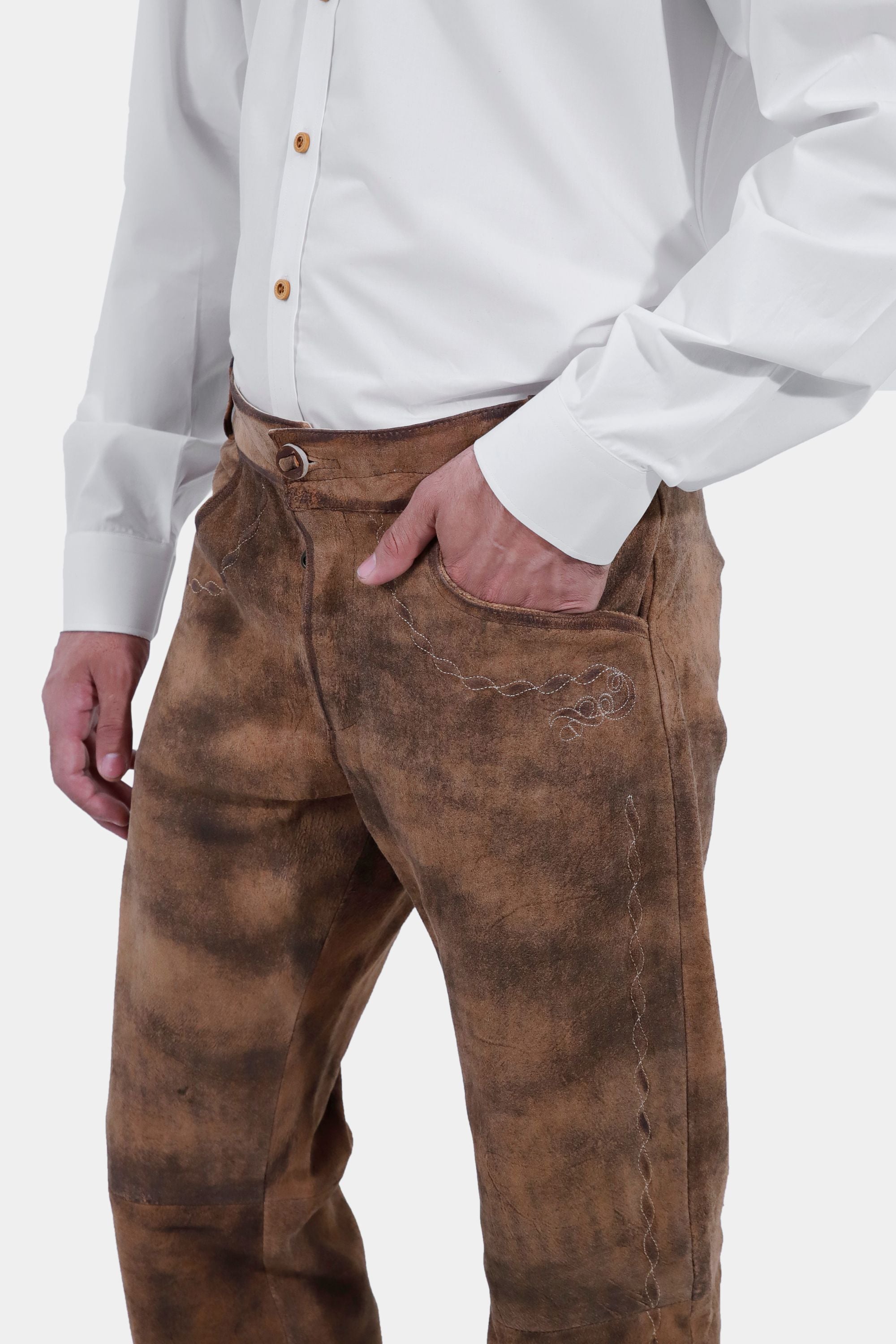 closed side view of a man wearing traditional lederhosen long pants with intricate embroidery paired with a plain white shirt and brown shoes