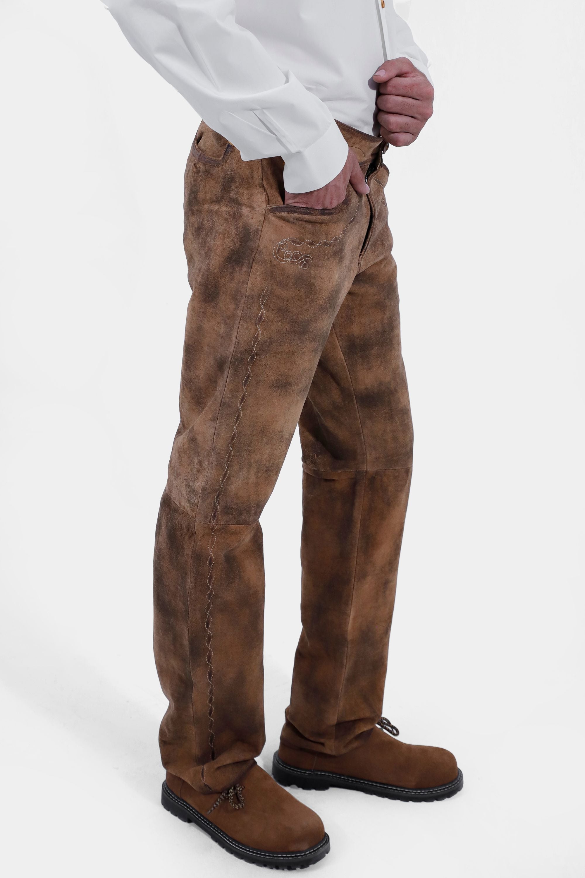 closed side view of a man wearing traditional lederhosen long pants paired with a plain white shirt and brown shoes