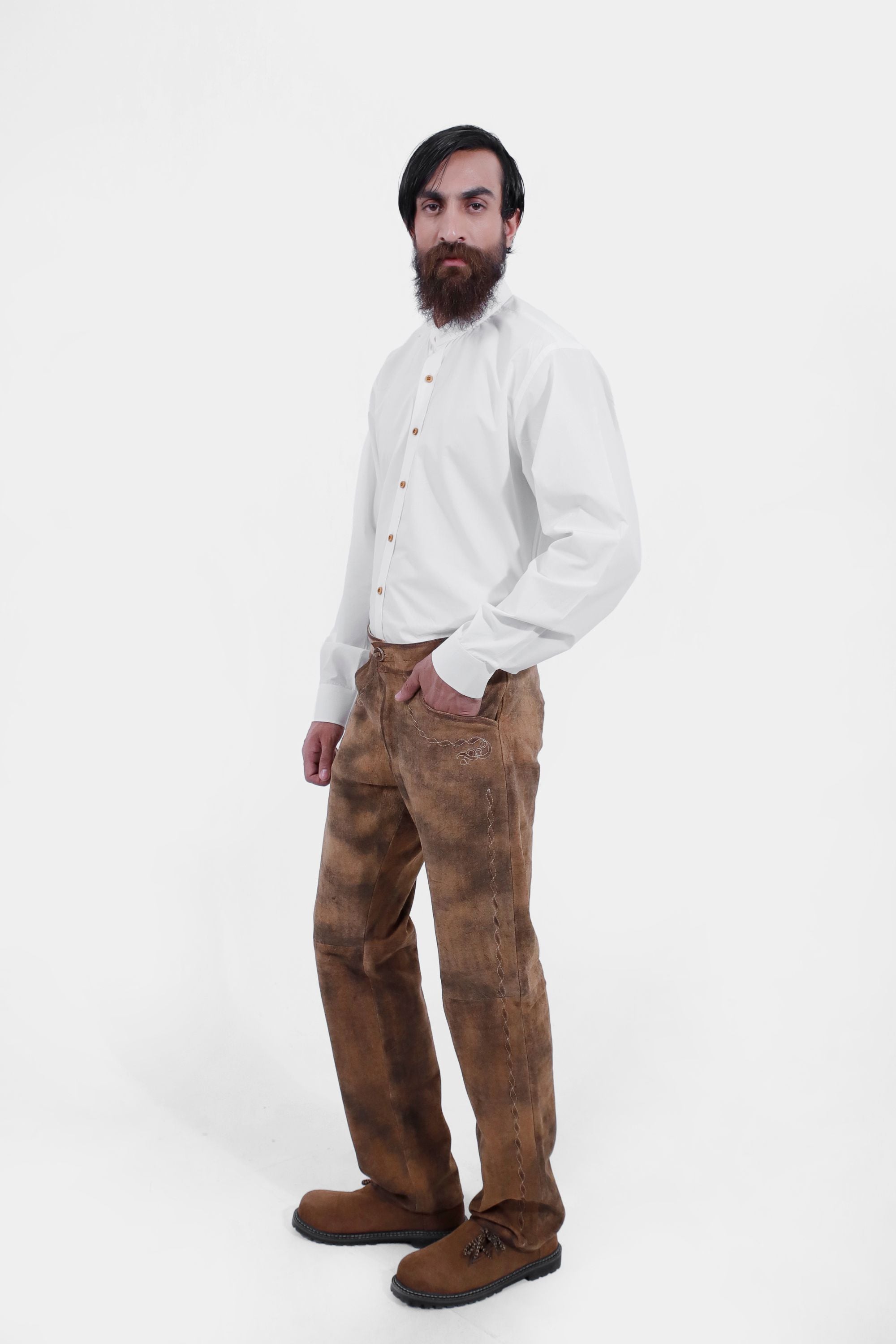 Side view of a man wearing traditional lederhosen long pants paired with a plain white shirt and brown shoes