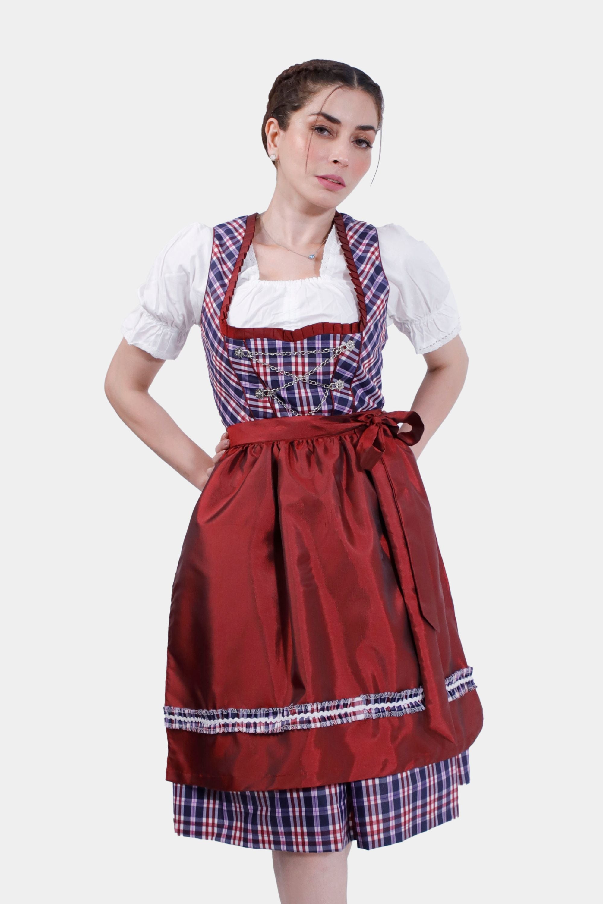 A woman wearing a "Dirndl Jentsch" with a red apron and plaid dress, paired with metallic heels, stands against a plain white background.