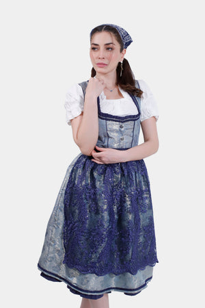 Woman wearing a traditional Dirndl dress in silver and blue, with a matching headscarf, posing with hand resting under her chin.