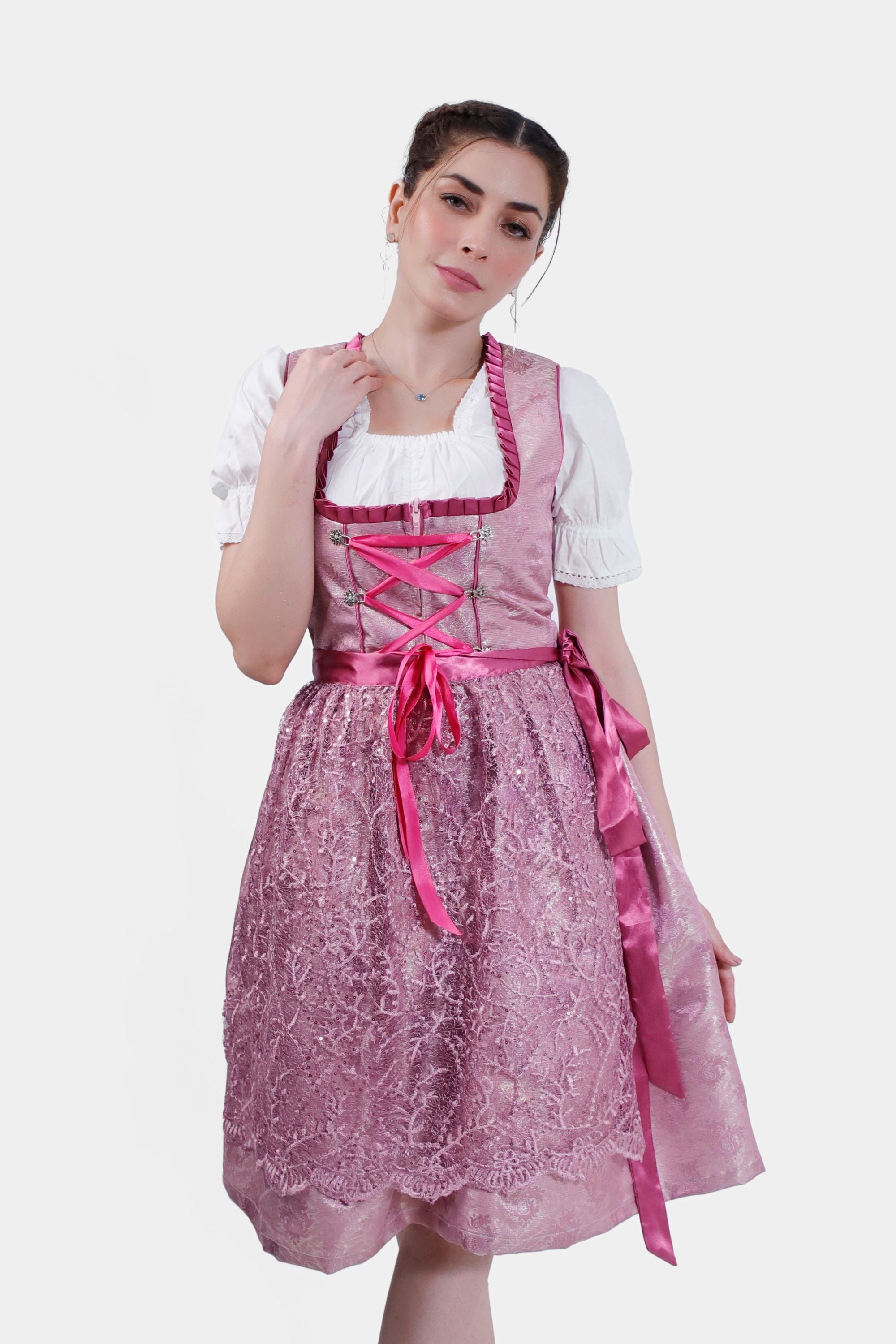 Front view of a model in a pink dirndl with a lace overlay, satin ribbon lacing, and a white blouse, paired with metallic high heels
