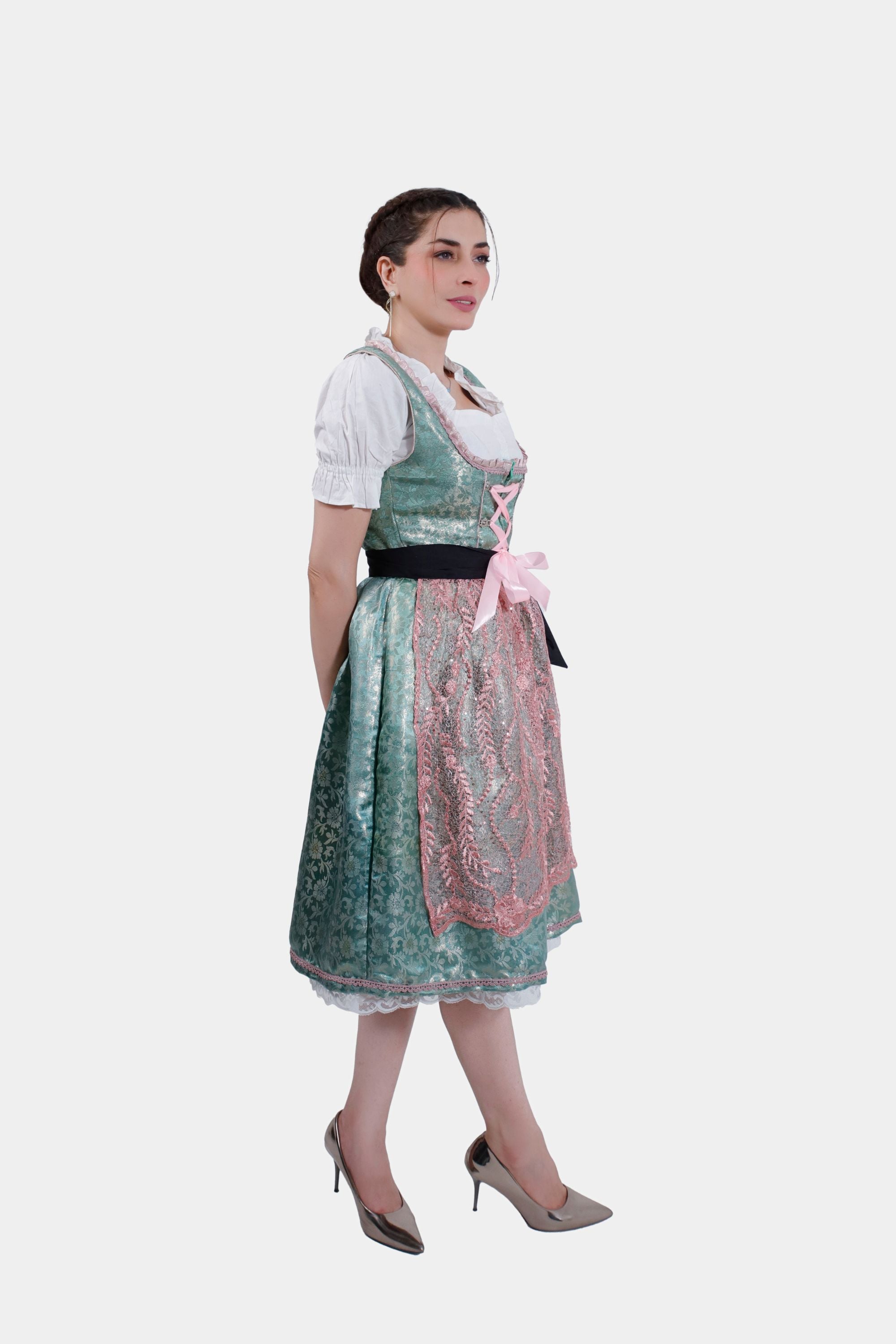 A side profile of the woman wearing the dirndl, looking over her shoulder. The green and pink colors of the dirndl stand out against the white background, with the black ribbon accentuating her waist.