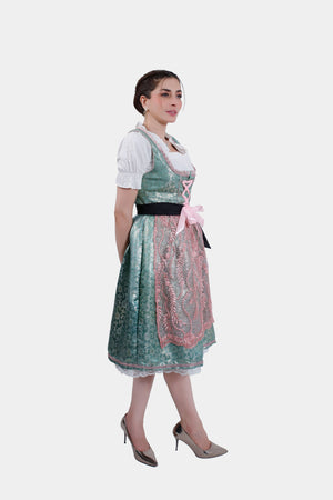 A side profile of the woman wearing the dirndl, looking over her shoulder. The green and pink colors of the dirndl stand out against the white background, with the black ribbon accentuating her waist.