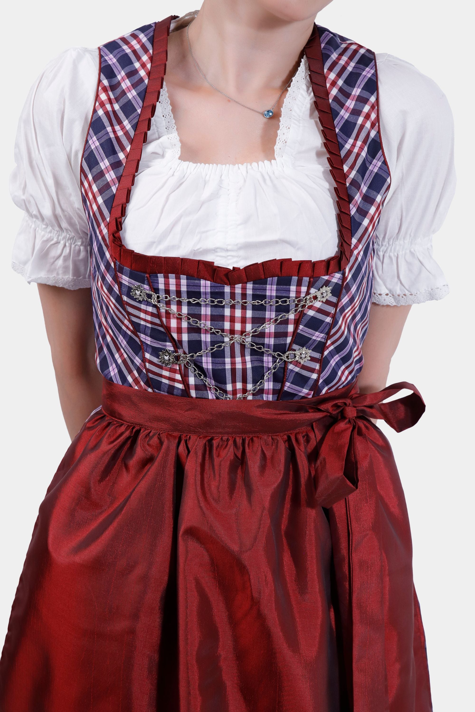 Close-up of the dirndl bodice showing intricate lace detailing on the neckline and silver chain embellishments over the plaid fabric