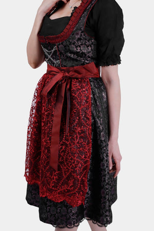 Side view of the dirndl, highlighting the intricate red embroidery on the apron and the black patterned fabric of the skirt.