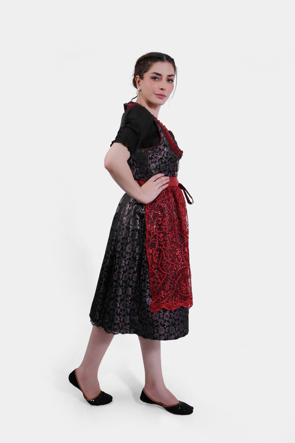 Side profile of the woman in the dirndl, her hands resting on her hips, displaying the rich textures and patterns of the outfit.