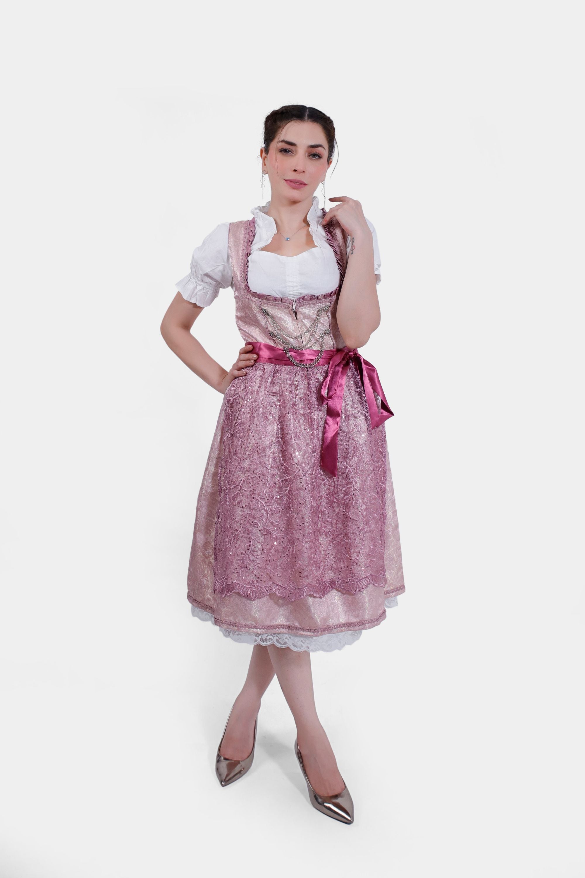 Full-length image of the model in a pink dirndl dress with a lace-trimmed apron, styled with metallic heels and a white blouse.