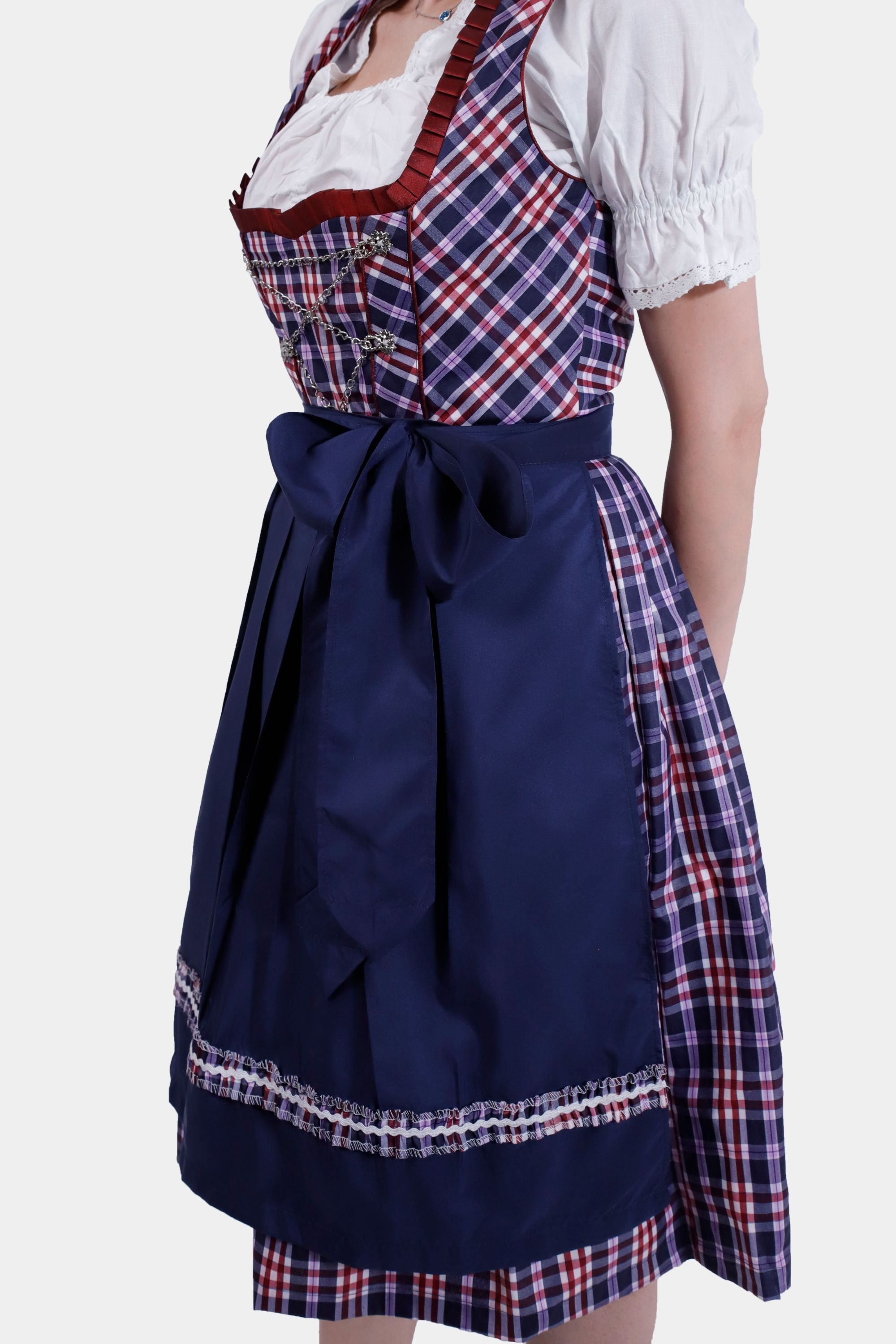Side view of the woman in the Dirndl dress, highlighting the navy blue apron and the full skirt with a plaid underlay. The white blouse sleeves are puffed, adding to the traditional Bavarian look.