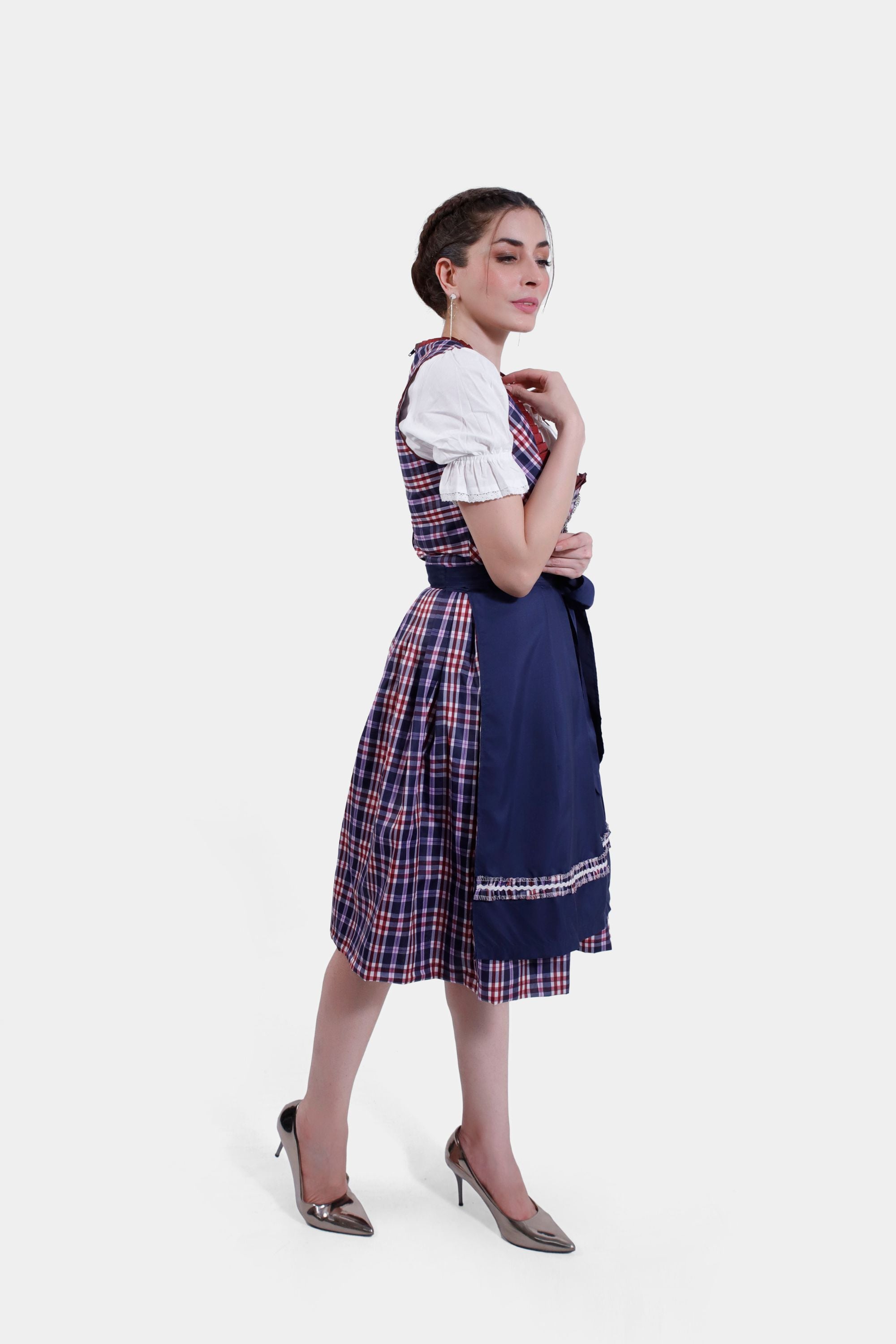 Side profile of the woman in the Dirndl dress, with a focus on the fit of the bodice and the flow of the skirt. The outfit is complemented by a pair of shiny metallic heels, completing the traditional yet stylish ensemble.
