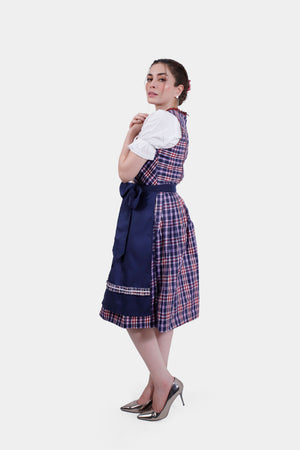 Side profile of a woman in a navy blue and plaid Dirndl dress with a white blouse, showing the back detail and a tied waist bow, paired with metallic heels.