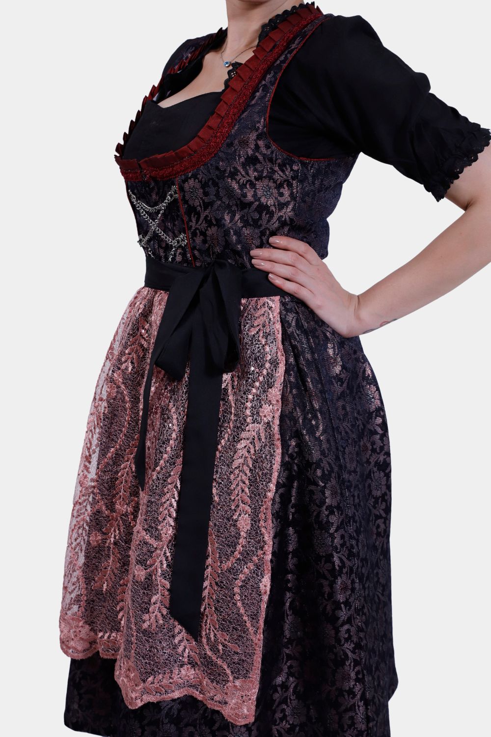 Side view of the dirndl dress, highlighting the black bodice with red trim, tied pink lace apron, and intricate floral patterns on the skirt.