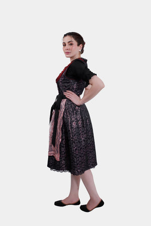 A side profile of the dirndl dress, emphasizing the contrast between the black bodice and the pink lace apron over the floral-patterned skirt.