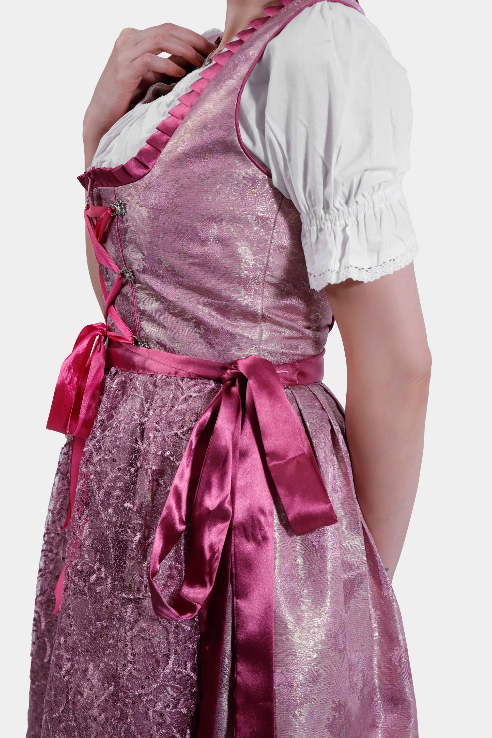 Side view of the model in a pink dirndl, highlighting the fitted bodice, lace overlay, and satin ribbon tied at the waist.