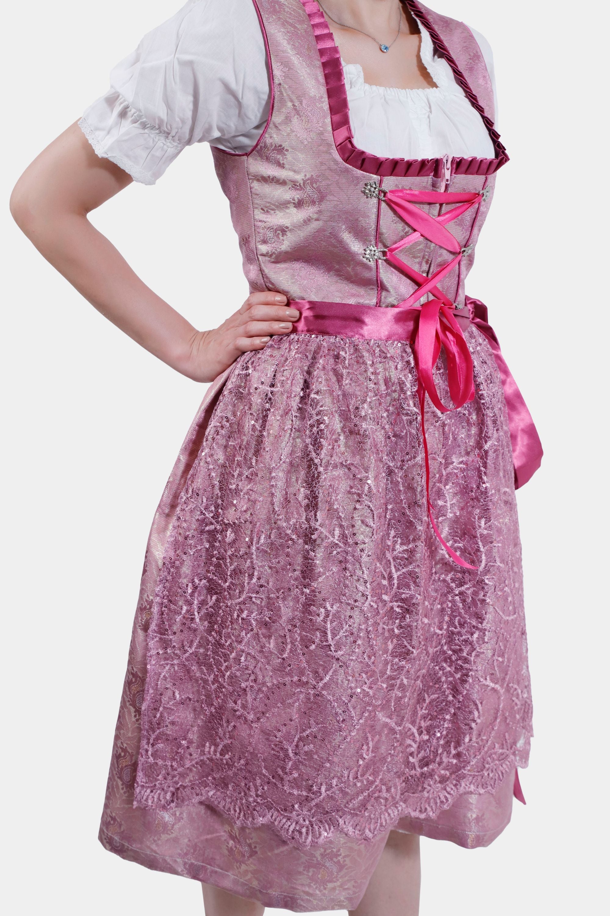 Detail shot of the lace skirt and pink satin ribbon on the pink dirndl, paired with the white blouse's puffed sleeves.