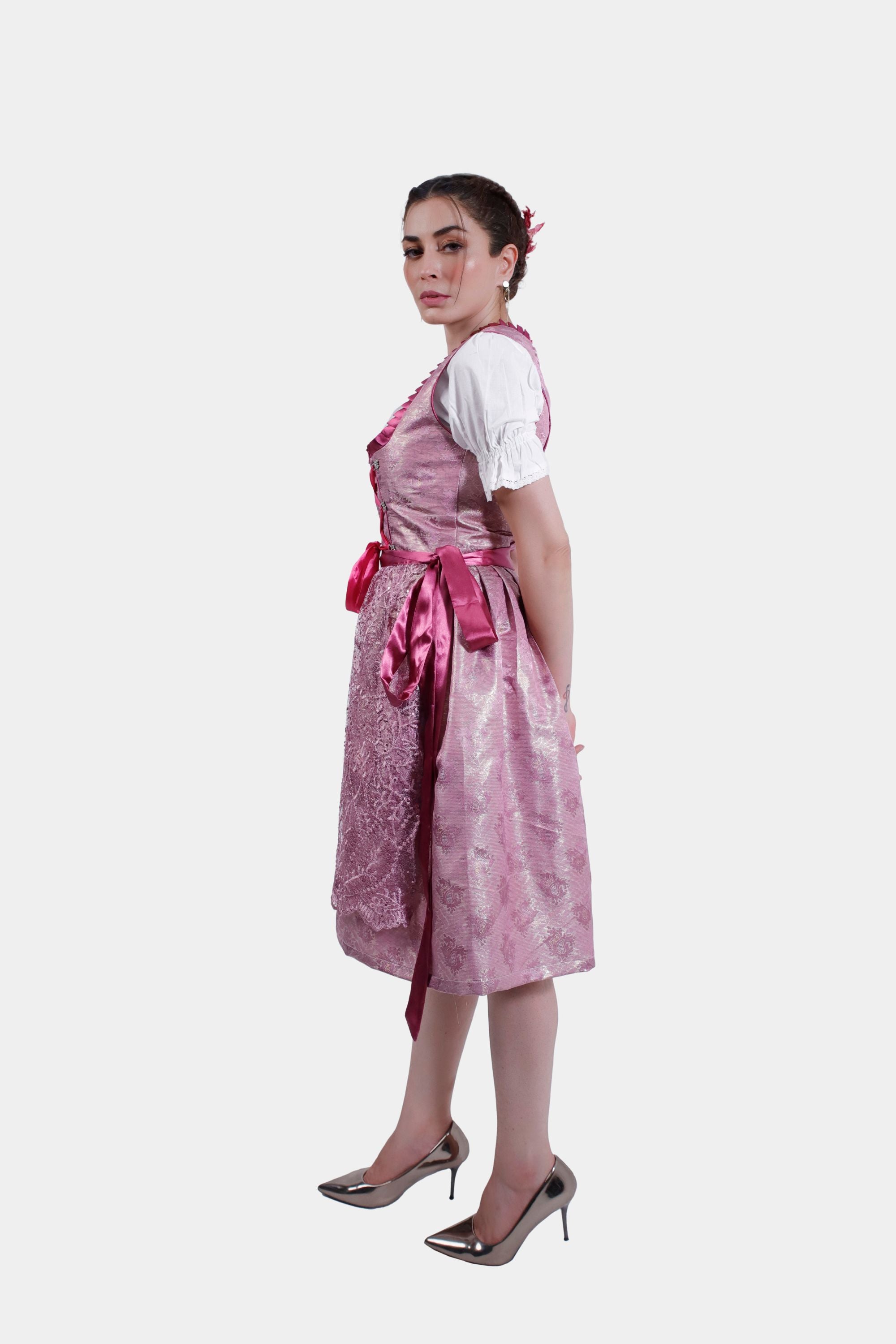 Angled front view of the pink dirndl, showing the intricate lace overlay on the skirt and the satin ribbon lacing on the bodice.