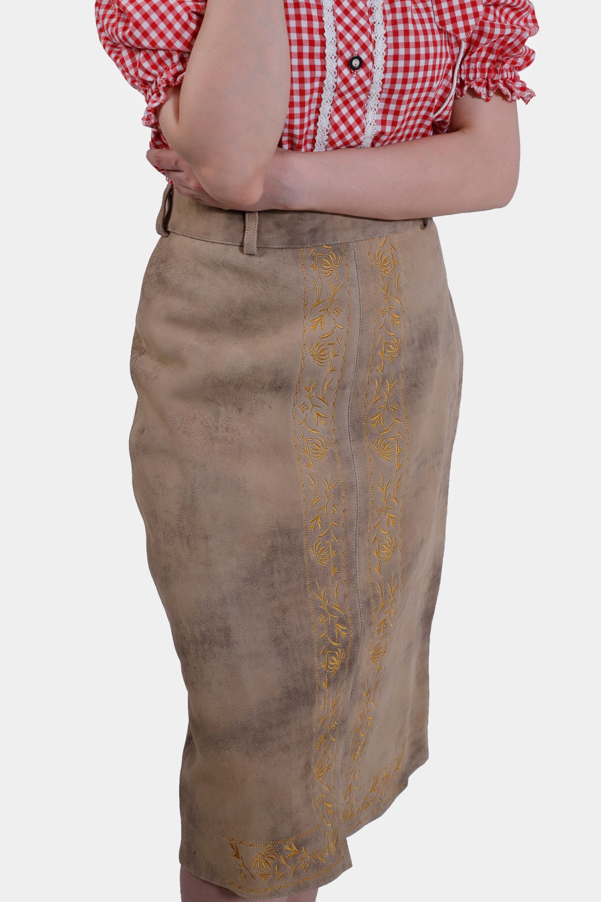 Close-up view of the beige leather skirt featuring intricate yellow embroidery along the front panel. The woman is partially visible, showing her red and white checkered blouse.