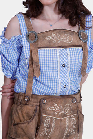 Close-up of a woman in a blue and white checkered off-shoulder top with ruffled details and light brown suede lederhosen, focusing on the intricate embroidery on the lederhosen.