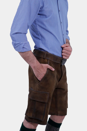 Closed Side view of a man in a blue striped shirt is posing in traditional brown leather cargo Lederhosen. The outfit is accessorized with a belt and traditional Bavarian socks and shoes. The side view showcases the side pockets and the decorative belt buckle.