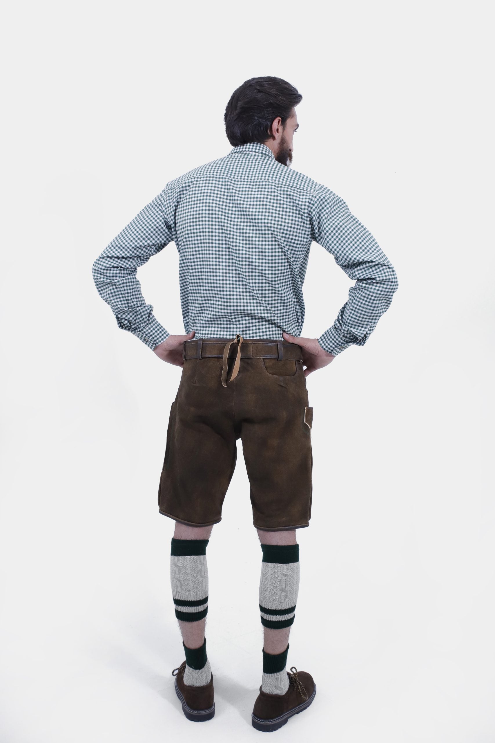 Rear view of a man wearing Geneva Lederhosen, displaying the detailed embroidery on the back of the brown leather shorts, complemented by a blue and white checkered shirt and green socks.