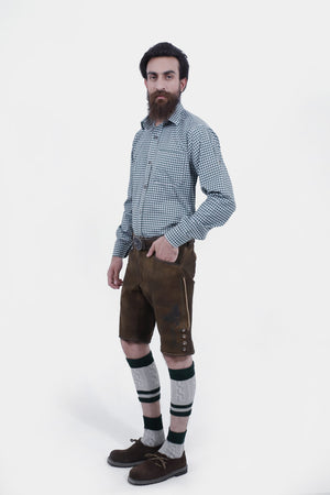 Full-length sidr view of a bearded man dressed in Geneva Lederhosen, featuring a green and white checkered shirt, rich brown leather shorts with embroidery, green socks, and sturdy brown shoes.
