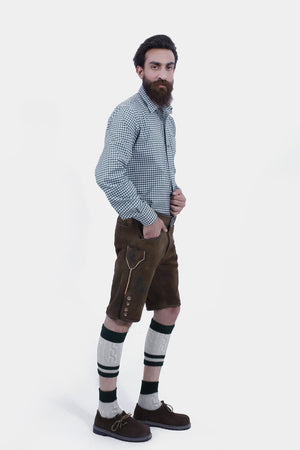Full-length view of a bearded man dressed in Geneva Lederhosen, featuring a green and white checkered shirt, rich brown leather shorts with embroidery, green socks, and sturdy brown shoes.