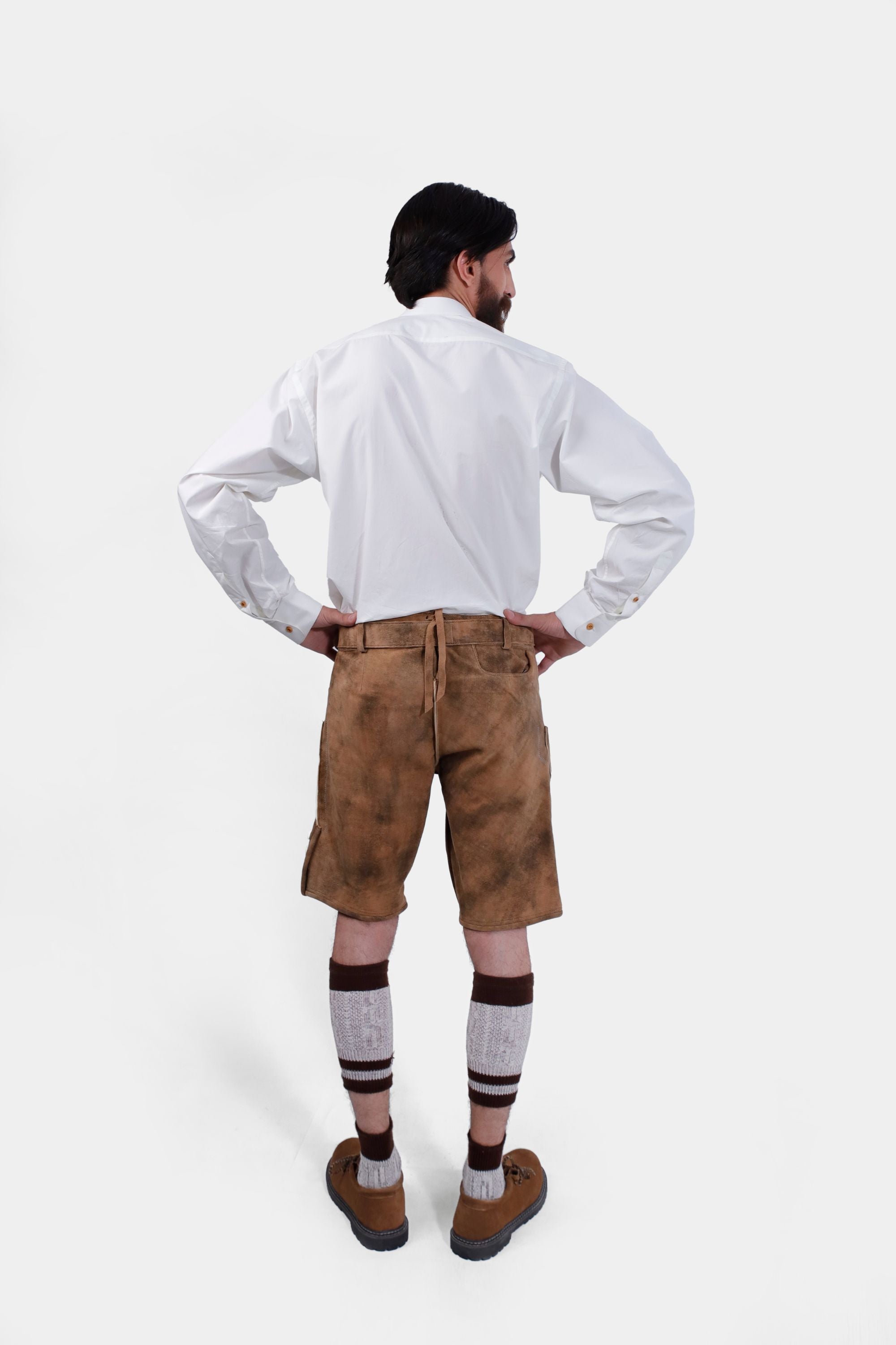 back view of a bearded man standing confidently in Gerd Muller Lederhosen, complete with knee-high socks and traditional shoes.