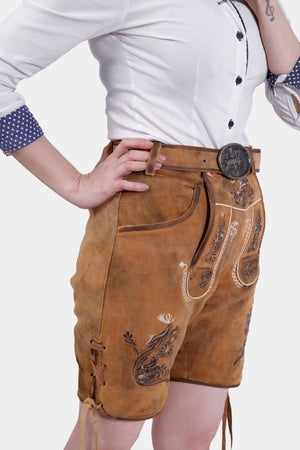 Side view of the Hedy Lamarr Lederhosen showing the side knife pocket and intricate embroidery on the legs. The model pairs it with a white blouse with polka dot accents.