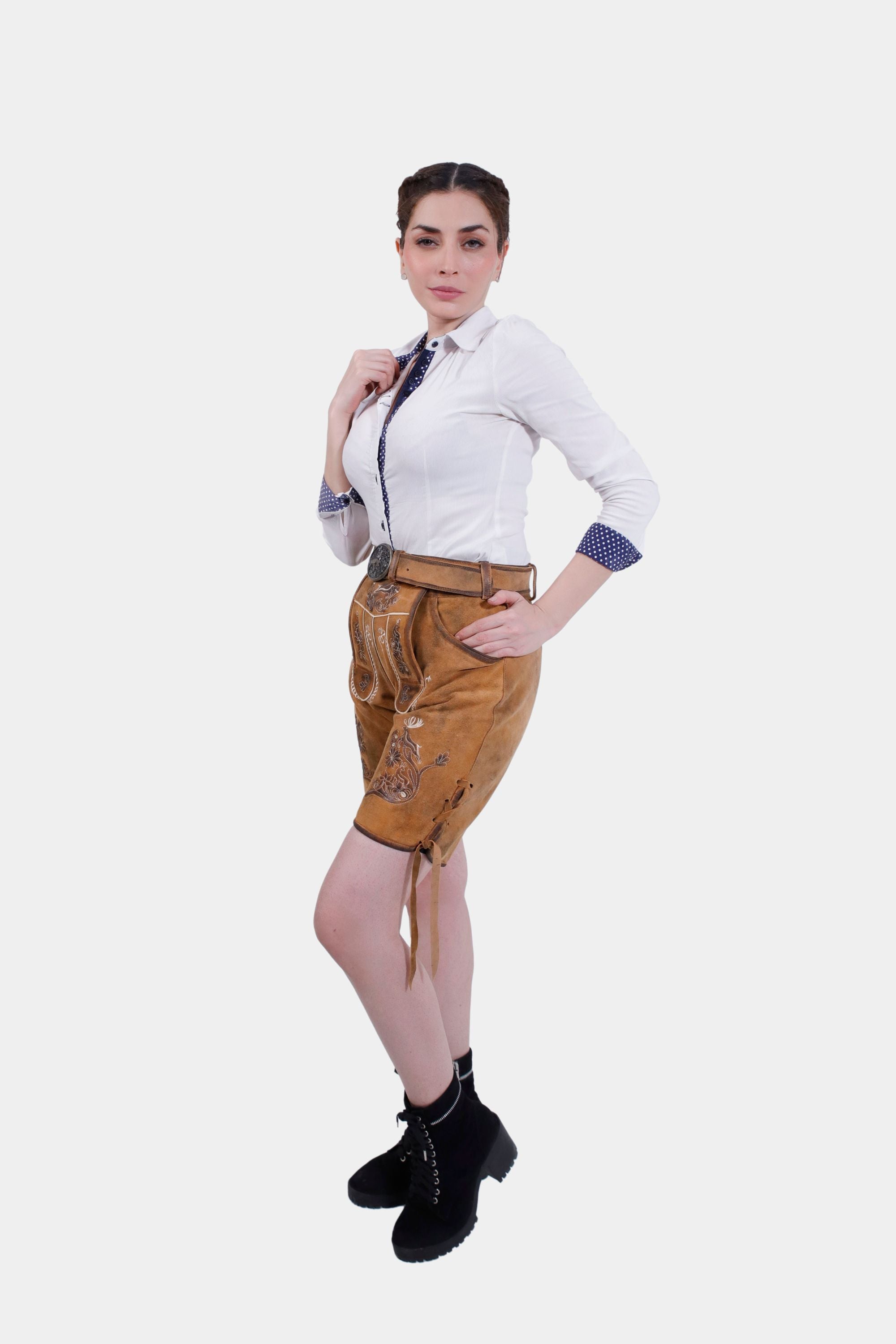 Full-body view of a woman wearing Hedy Lamarr Lederhosen and a white blouse with polka dot accents. The Lederhosen feature white embroidery and laces at the cuffs, styled with black ankle boots.