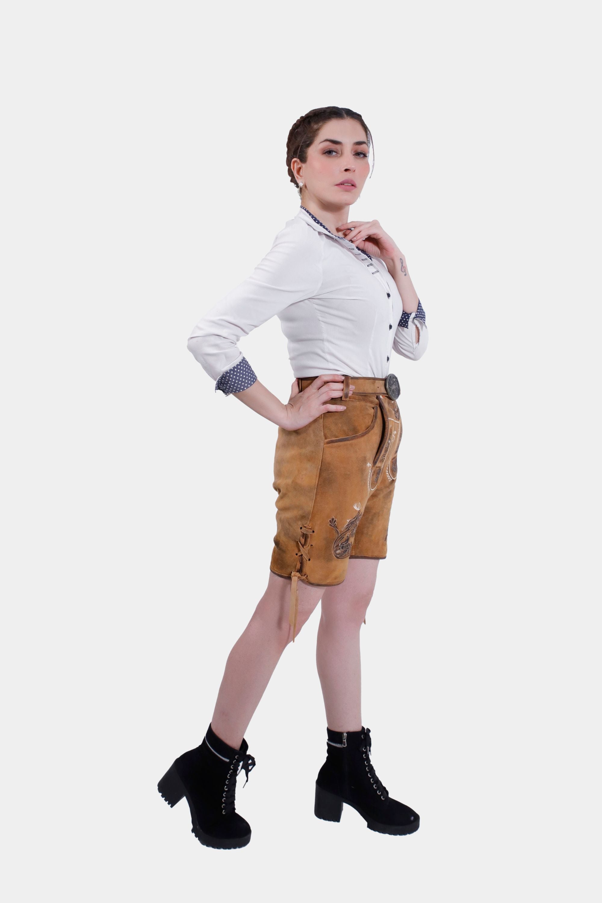 Side profile of the Hedy Lamarr Lederhosen showcasing the side knife pocket and detailed embroidery. The model wears a white blouse with polka dot accents, emphasizing the fit and style of the Lederhosen.