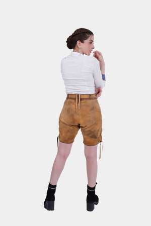 Rear view of the Hedy Lamarr Lederhosen showing the back pocket and adjustable waistband with laces. The model wears a white blouse with polka dot accents, providing a full view of the Lederhosen's fit and design.