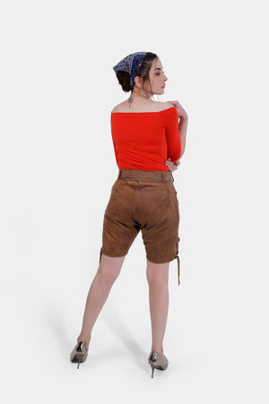 Full-body back view image of a woman wearing Heidi Klum Lederhosen, displaying the back details and adjustable waistband, paired with a bright red off-the-shoulder top and a blue bandana.