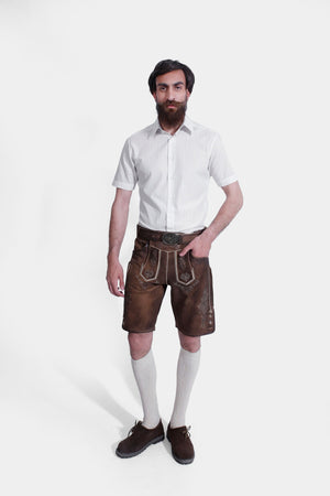 full-body view of the man showing the white shirt and brown lederhosen paired with cream-colored knee-high socks and brown shoes.