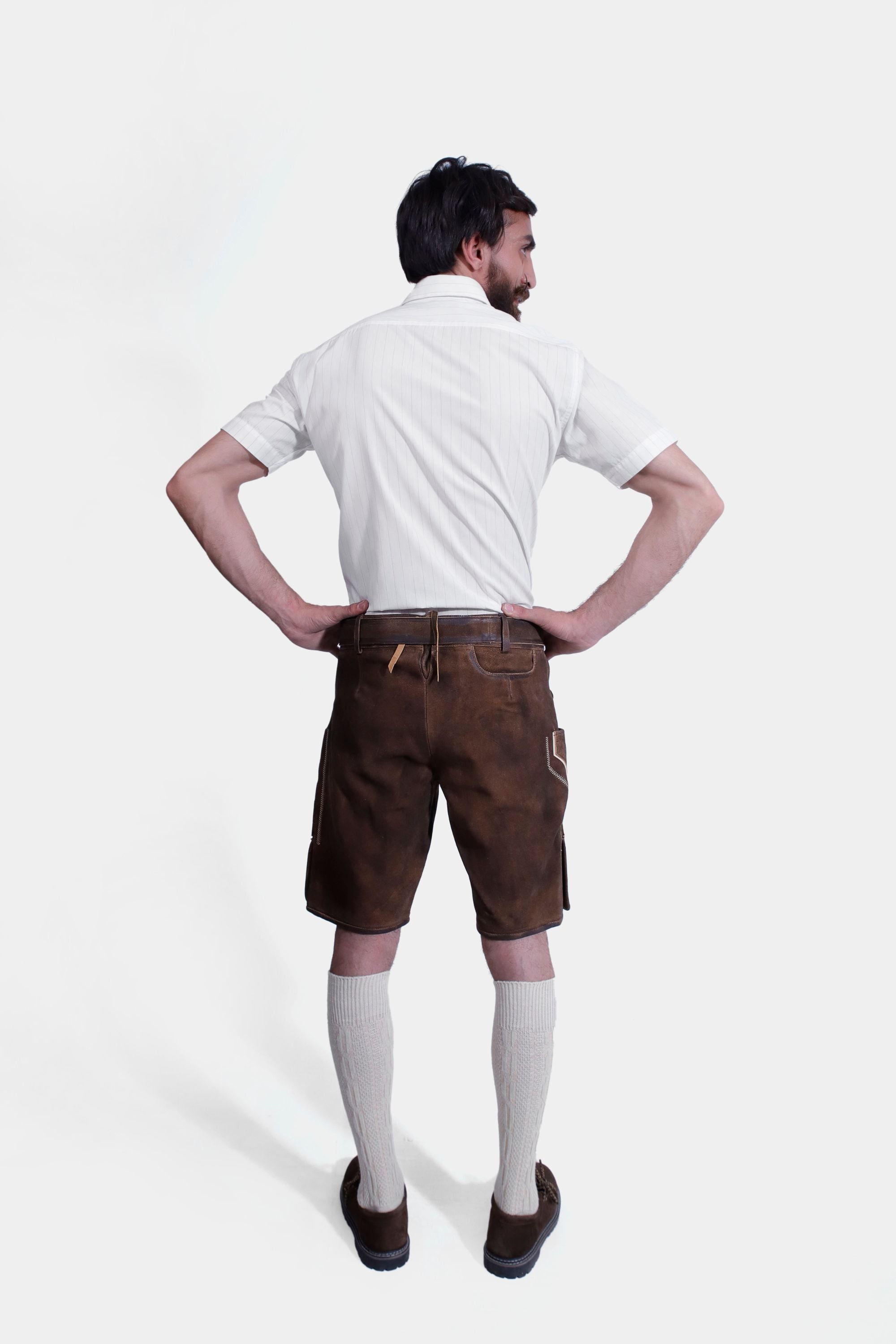 The man poses from the back, displaying the fit and stitching details of the brown lederhosen.