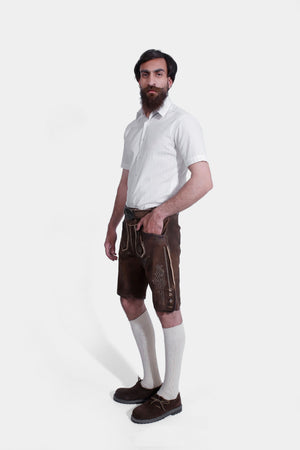 A front side view of the man wearing the brown leather lederhosen with suspenders, paired with the white shirt.