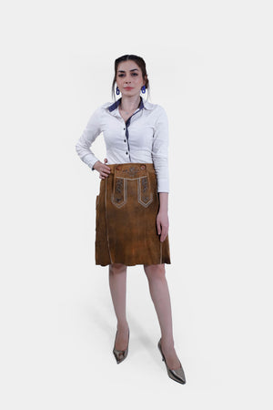 A full-body shot of a woman wearing a white shirt and a brown leather Jennifer Lederhosen Skirt with intricate embroidery, standing with one hand on her hip.