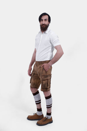 side view of a man wearing brown leather cargo lederhosen and a short-sleeved white shirt. The man has his right hand in the pocket, highlighting the detailed stitching and buttons on the lederhosen.