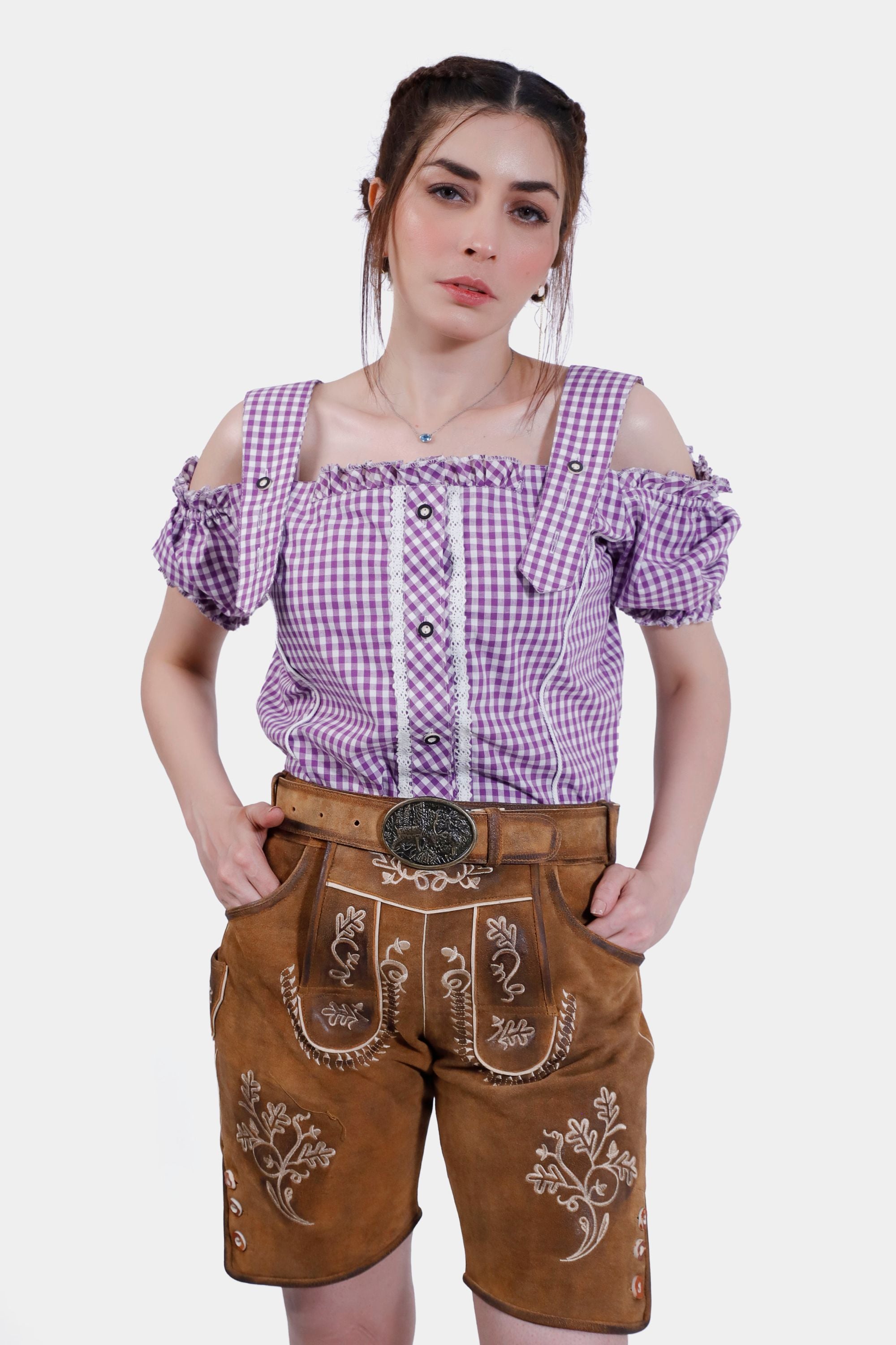 Model wearing traditional brown leather lederhosen shorts paired with a purple checkered blouse with off-the-shoulder sleeves and a decorative belt.