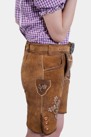 Side view of a model in brown leather lederhosen shorts with white embroidery, showcasing the side pocket and button detailing, paired with a purple checkered blouse