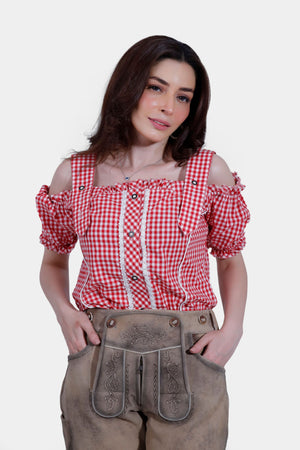 Close-up view of the woman in a red and white checkered off-shoulder blouse and light brown lederhosen pants, highlighting the detailed embroidery on the bib and suspenders.