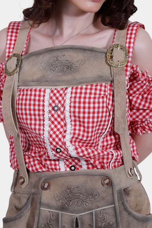 Close-up view of the woman in a red and white checkered off-shoulder blouse and light brown lederhosen pants, highlighting the detailed embroidery on the bib and suspenders.
