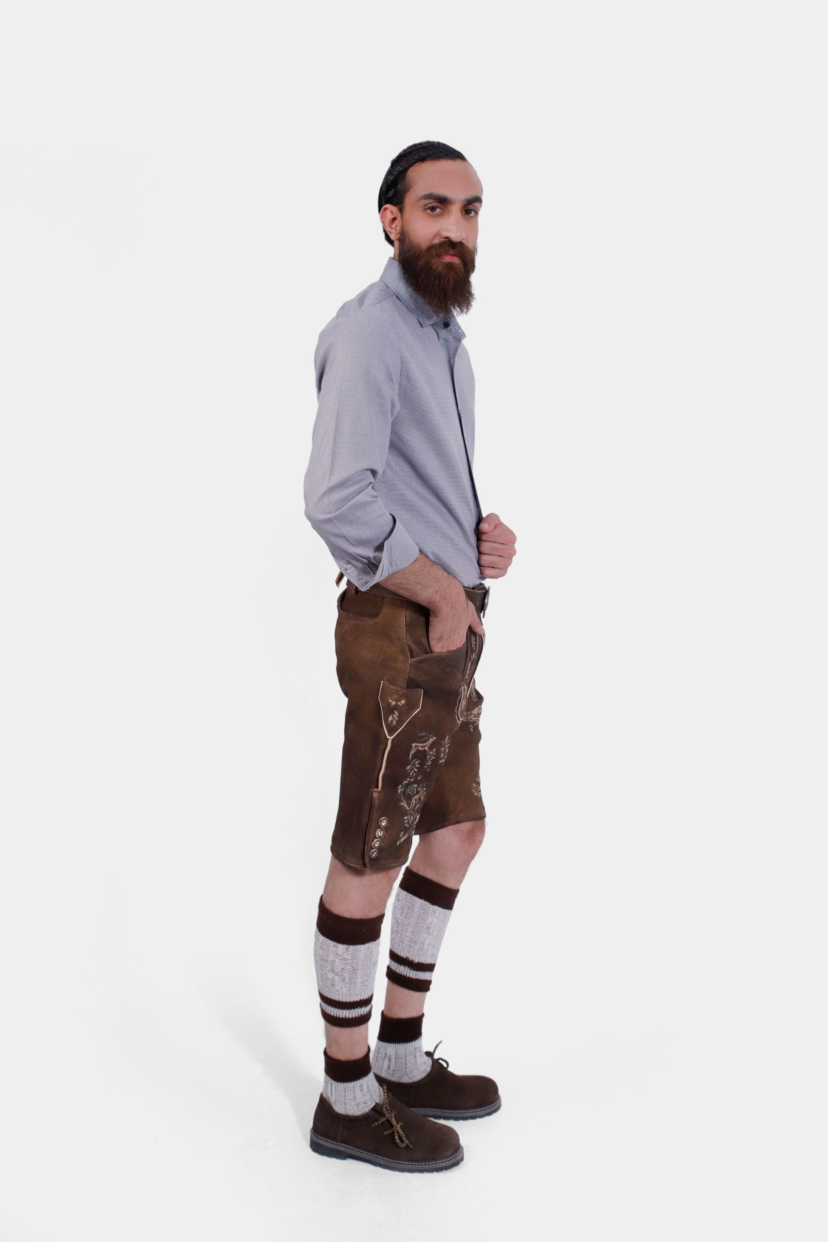 Side view of the man in Lederhosen, grey shirt, knee-high socks, and traditional shoes, standing with a neutral expression.