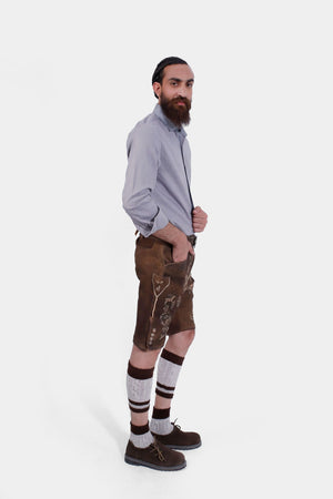 Side view of the man in Lederhosen, grey shirt, knee-high socks, and traditional shoes, standing with a neutral expression.