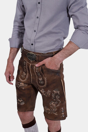 A man wearing a traditional grey shirt with brown Lederhosen, detailed with intricate embroidery and a decorative belt buckle.