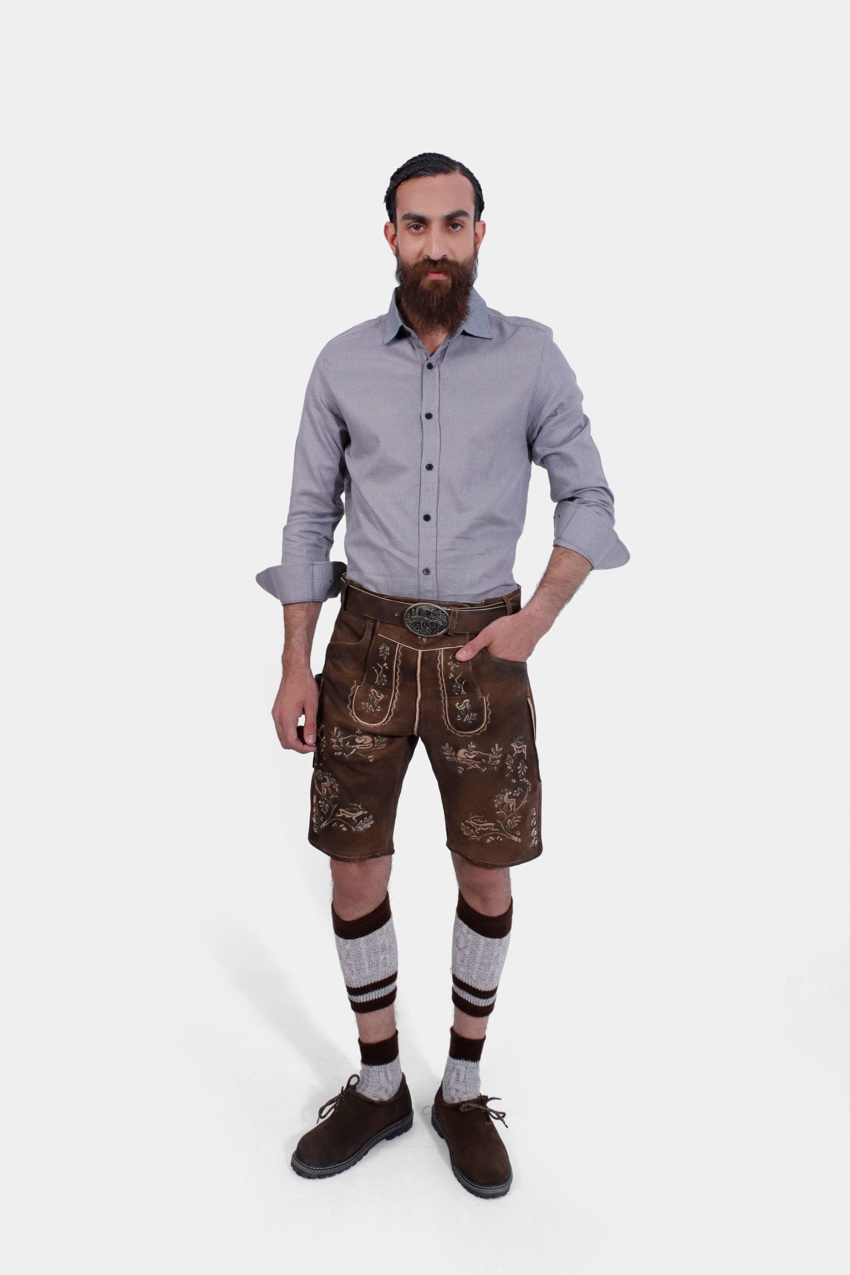 Complete view of the man in Lederhosen, grey shirt, knee-high socks, and traditional shoes, standing with a neutral expression.