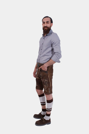 Side view of the man in Lederhosen, grey shirt, knee-high socks, and traditional shoes, standing with a neutral expression.