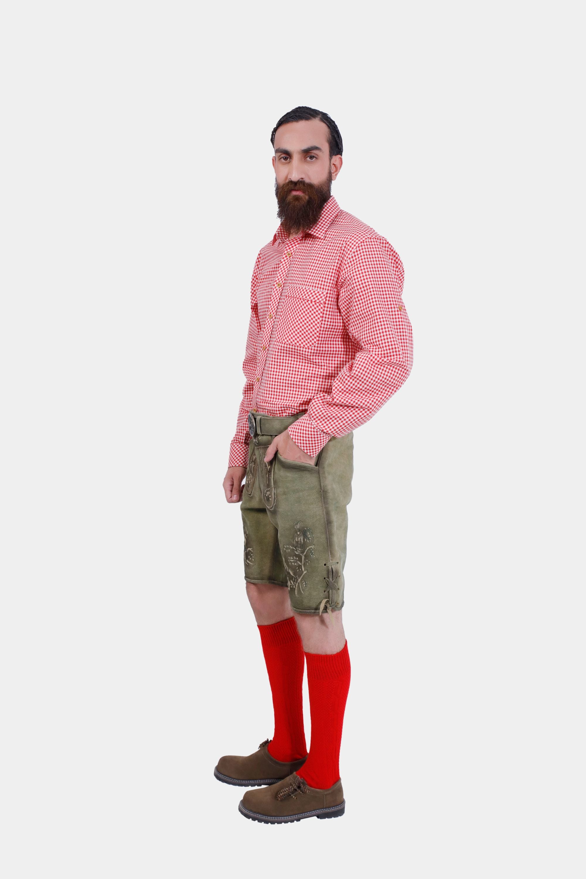 A man with a beard wearing a red checkered shirt, green embroidered Lederhosen, red knee-high socks, and brown shoes, standing sideways against a white background.